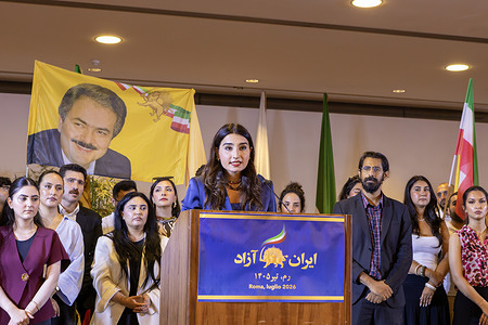 A young woman delivers a speech from the podium as participants stand on stage under a banner during the rally calling for a secular, non-nuclear republic in Iran. Iranians in exile and prominent international figures gathered for a rally in Rome demanding an end to executions and the establishment of a democratic republic in Iran. National Council of Resistance of Iran (NCRI) President-elect Maryam Rajavi addressed the crowd via video message, presenting her Ten-Point Plan for a secular, non-nuclear Iran. Speeches by prominent figures highlighted that internal resistance, rather than external intervention, drives true change.