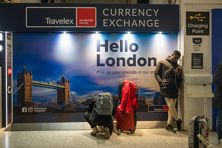 People seen in front of a sign reading "Hello London" at Stansted Airport.