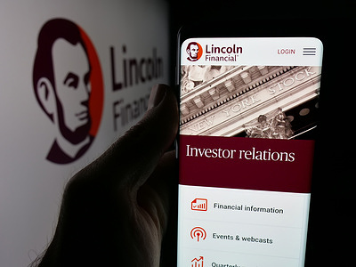 In this photo illustration, a person is holding a smartphone with the web page of US insurance company Lincoln Financial Group on screen in front of logo.