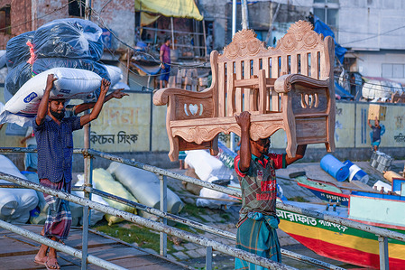 Labourers carry goods to load on a boat along river Buriganga in Dhaka.