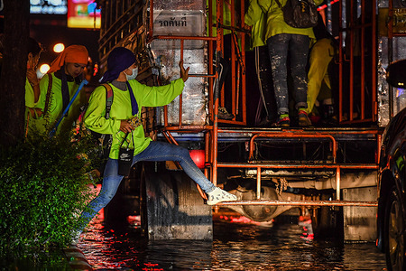 Construction workers Try to step on the bus through a flooded street during a heavy rainfall.