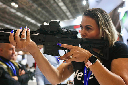 A Brazilian woman tries out one of the latest weapons at the stands of LAAD, Latin America's largest defense and security trade fair More and more Brazilian women are buying guns to ensure their safety or to practice sports shooting, convinced by industry lobbying and ex-president Bolsonaro.