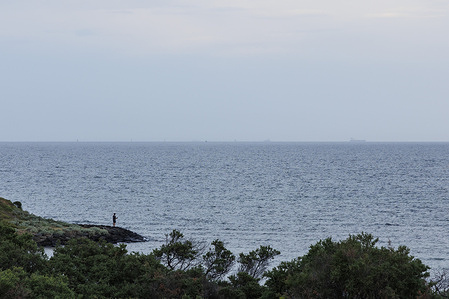 A man is seen fishing off the rocks from Green Point in Brighton ahead of a severe day of weather for Melbourne which threatens to reach a top of 42 degrees and brings a total fire ban as bushfires burn across the states north.