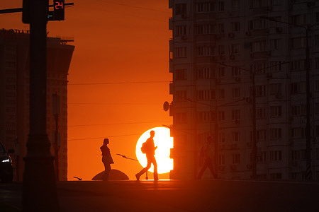 Pedestrians cross a street against a setting sun in the Zyuzino district in Moscow.