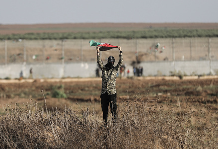 A Palestinian holds a flag near the Gaza-Israel barrier during the demonstration marking the 2005 Israeli withdrawal from Gaza. Palestinian protesters held a demonstration at the Israel-Gaza Border to commemorate the "2005 Israeli disengagement from Gaza". The protest escalated into clashes between the protesters and the Israeli military. The "2005 Israeli disengagement from Gaza" is the dismantling of 21 Israeli settlements and the evacuation of over 8,000 settlers and the Israeli army from the Gaza Strip in 2005.