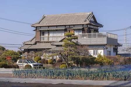 Traditional Japanese style house surrounded by fields inside an agricultural area in Yokohama. "Small-scale agriculture in Yokohama thrives as a form of urban farming within Japan's second-largest city, where farmland covers about 7-8% of the area despite dense urbanization. The focus is on recreation, food education, local freshness, preserving green space against development, and sustainability — not large commercial output. Demand is high, with many gardens having waitlists, reflecting urban residents' interest in hands-on growing and nature connection."