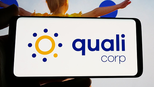 In this photo illustration, a person is holding a cellphone with the logo of Brazilian health insurance company Qualicorp SA on screen in front of website.