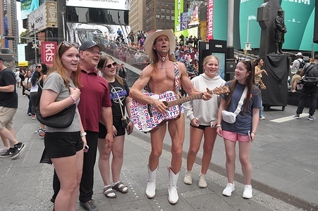 Street performer, Robert Burck, also known as the Naked Cowboy, poses for a photo with pedestrians in Times Square, Manhattan, New York City.