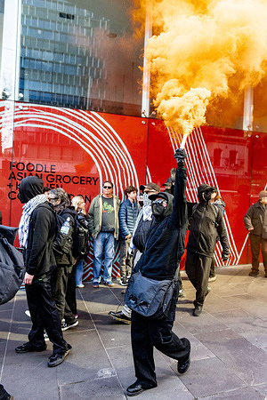 A masked pro-trans rights protester lights a smoke flare during a counter-demonstration against the “Women Will Speak” rally. Police used traffic barriers to form lines to separate opposing groups during protests outside the Victorian Parliament. Trans rights activists rallied to counter a “Women Will Speak” event, accusing organisers of promoting anti-trans views, while attendees of the women’s rights rally defended their platform as free speech. Demonstrators on both sides waved flags, held placards, and chanted as officers managed crowd movements, questioned participants, and made arrests after clashes. The tense standoff drew hundreds, highlighting deep divisions over gender rights and public discourse in Australia.