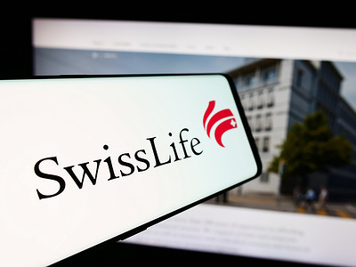In this photo illustration, a person holds a mobile phone with the logo of insurance company Swiss Life Holding AG in front of business webpage.