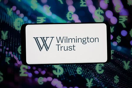 In this photo illustration, the logo of US financial business Wilmington Trust Co. is displayed on a smartphone in front of abstract background on computer screen.