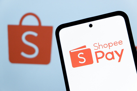 In this photo illustration, the ShopeePay (Shopee Pay) logo is seen displayed on a smartphone screen and Shopee logo in the background.