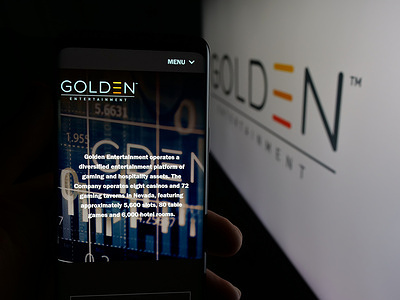 In this photo illustration, a person is holding a cellphone with the webpage of US gaming company Golden Entertainment Inc. on screen in front of logo.