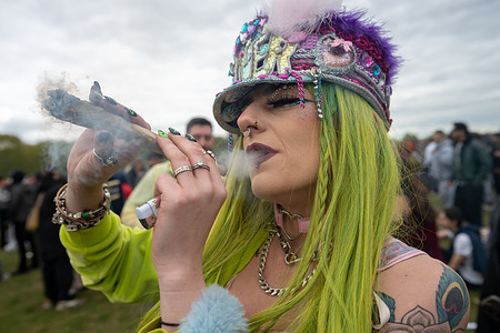 A woman seen smoking an oversized cannabis cigarette. Crowds gather in Hyde Park for the annual “420” event, an informal gathering associated with cannabis culture, where participants meet to socialise, advocate for drug policy reform, and publicly consume cannabis.
