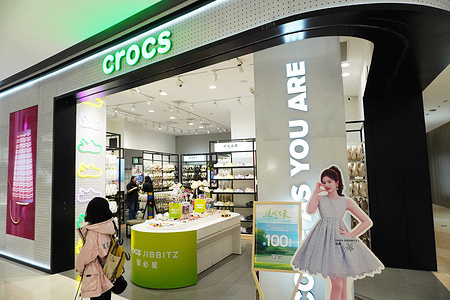 The Crocs store in Changzhou, showcases its bright green logo, neon shoe displays, and a promotional standee of a brand ambassador, with customers entering the shop.