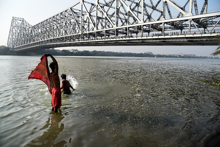 Locals seen taking bath next to the Howrah bridge in Kolkata.
The Rabindra Setu also known as the Howrah bridge is a bridge with a suspended span over the Hooghly River in Kolkata which was commissioned in 1943.
