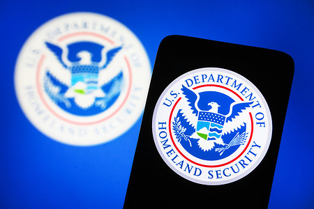 In this photo illustration, United States Department of Homeland Security (DHS) logo is seen on a smartphone and on a pc screen.