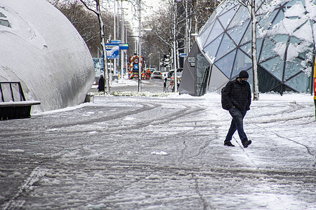 A man walks along a snow covered square.Rare April snowfall in Europe as cold winter weather returns after historic warm days. Day 3 of the snow in the Dutch city of Eindhoven.
