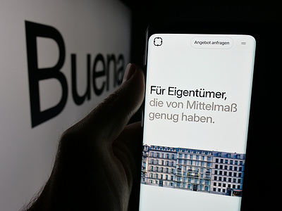 In this photo illustration, a person is holding a smartphone with the web page of German property management company Buena Gmbh on screen in front of logo.