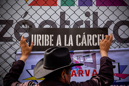 A demonstrator holds a banner that says: Uribe in prison during the rally. After 13 years, the Colombian justice system has found former President Álvaro Uribe Vélez guilty of abuse of process and bribery of a public official, exposing his links to paramilitary groups. During the 10-hour trial, a small group of Uribe supporters gathered outside the courthouse. Amid prayers, insults toward opposing demonstrators, and an attack on a photojournalist, the crowd gradually dispersed as their hopes diminished.