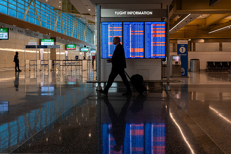 A traveler walks past a departures' board at Washington Reagan International Airport amidst flight delays and cancelations due to weather.