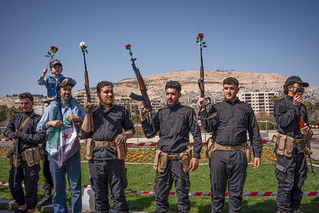 A group of Syrian army soldiers, former members of Hay'at Tahrir al-Sham 
 (HTS) raise their weapons with flowers on the tip of them during the celebration of the anniversary of the beginning of the Syrian revolution. Dozens of people take over Umayyad Square in Damascus, Syria to celebrate the beginning of the start of the revolution as a helicopter flew overhead dropping flowers.