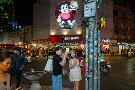 A couple takes selfies with a backdrop of a restaurant at an intersection on Banthat Thong street. The street has emerged as a food street for its nightlife and street vibe over the past few years.