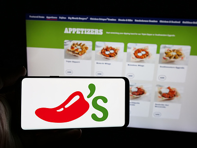 In this photo illustration, a person is holding a smartphone with the logo of US restaurant chain company Chilis Grill Bar on screen in front of website.