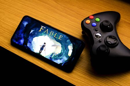 In this photo illustration, the Fable game logo is seen displayed on a smartphone screen next to an Xbox video game controller.