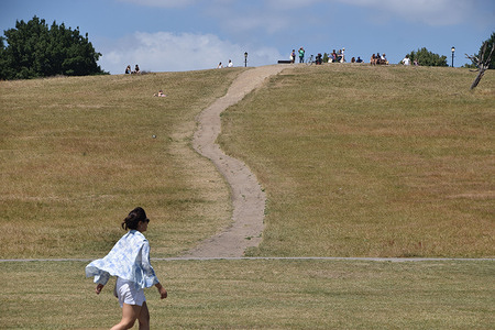 A woman walks along a very dry Primrose Hill as the UK heatwave continues.