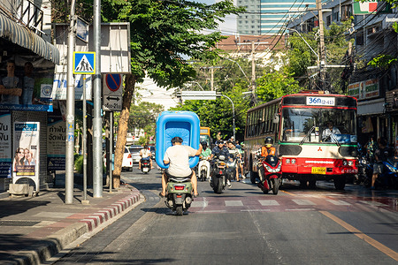 A woman sitting on the back seat of a motorbike is seen carrying an inflatable swimming pool through the street during the Songkran 2026 in the Huai Khwang community. Songkran is the Thai New Year celebration, symbolizing cleansing, renewal, and respect for elders through the ritual of pouring water to wash away bad luck and welcome a fresh start.