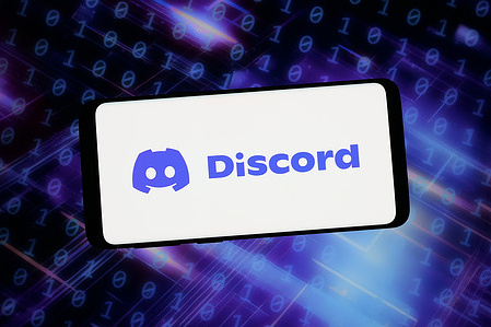 In this photo illustration, the logo of messaging and social media platform Discord is displayed on a smartphone in front of abstract background on computer screen.