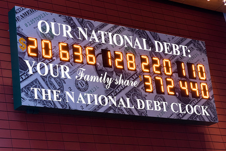 The National Debt Clock is a very very large digital display of the current gross national debt of the United States. It is mounted on a western facing wall in a wide covered alley in the middle of the block and runs between West 42nd Street and West 43rd Street. The alley is located between Sixth Avenue and Broadway in New York City. The displayed debt shown is as of March 23, 2018 when this image was created.