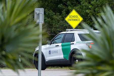 A U.S. Customs and Border Protection vehicle patrols the Overseas Highway near the entrance of a school.