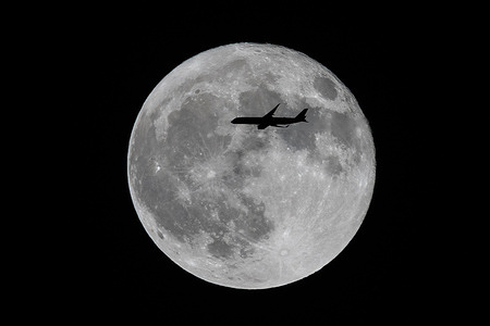 An airplane flies past the super blue full moon in Los Angeles.