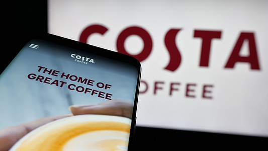 In this photo illustration, a mobile phone with the website of coffeehouse chain company Costa Coffee is seen on screen in front of logo.