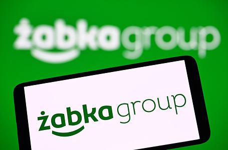 In this photo illustration, the Zabka Group logo is seen displayed on a smartphone and in the background.