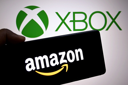 In this photo illustration, an Amazon logo is seen displayed on a smartphone with the XBox logo in the background.