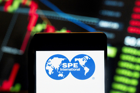 In this photo illustration, the Society of Petroleum Engineers (SPE) logo seen displayed on a smartphone with an economic stock exchange index graph in the background.