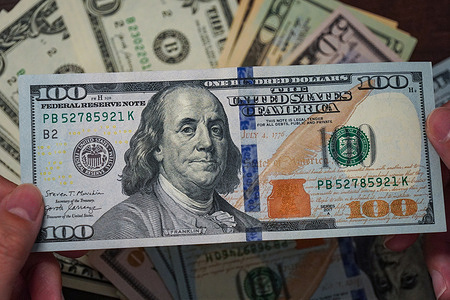In this photo illustration, a $100 bill seen displayed with the Federal Reserve seal, serial number against a backdrop of scattered bills.