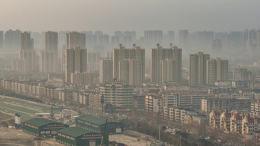 (EDITORS NOTE: Image taken with drone) 
View of a construction site with temporary green shelters occupies the foreground, while a row of uniform, modern high-rise buildings towers above older neighborhoods in the hazy morning light.