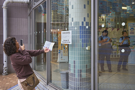 A voter takes a photo of her voting certificate in front of a polling station and police officers are monitoring the smooth running of the elections in Tin Shui Wai. The 2025 Hong Kong Legislative Council general elections, are taking place on December 7, 2025, to elect the 90 members of the 8th Hong Kong Legislative Council.