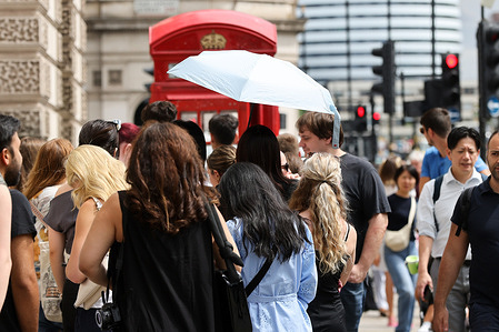 A woman shelters under an umbrella in Westminster, during warm and sunny weather in London.