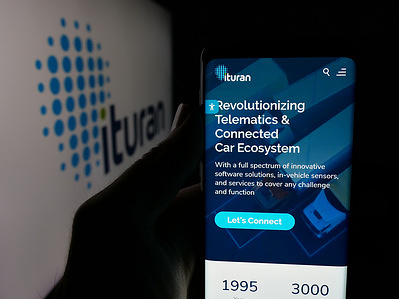 In this photo illustration, a person is holding a smartphone with the webpage of company Ituran Location and Control Ltd. on screen in front of logo.