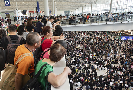 Travelers watch hundreds of anti government protesters staged a sit in protest at the Hong Kong international airport terminal, the first of three straight days of demonstrations after clashes last week triggered fears that a wider confrontation could erupt in the city