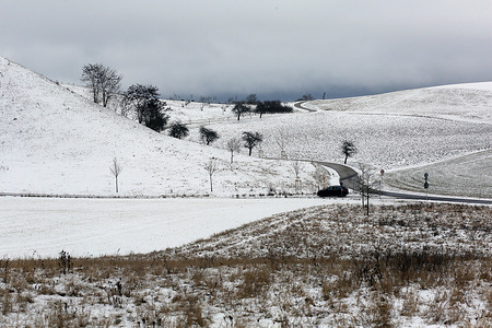 A car seen driving slowly up a country road. The day started with difficult travel conditions and reports of cancelled trains and accidents. In many places rain has started to fall which may lead to very dangerous roads. A mixture of rain and snow is forecasted for in many parts of the country.