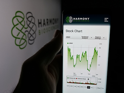 In this photo illustration, a person is holding a smartphone with the webpage of US company Harmony Biosciences Holdings Inc. on screen in front of logo.