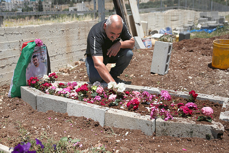 A Palestinian father Haroun Ashteh places a bouquet of flowers on the grave of his son Imad Haroun, 26 in the village of Salem. Imad Haroun was killed by Israeli border police while crossing the concrete separation barrier in search of work inside Israel between Jerusalem and the West Bank.
