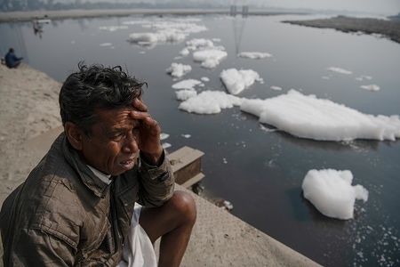 A local fisherman seated by the Yamuna river covered by froth from discharge of untreated industrial and domestic wastes, near Kalindi Kunj.
Yamuna river, often called Delhi’s lifeline, has been labelled as “ecologically dead” for its apparent incapability to regain its initial limpidness. Yamuna is overflowing with froth as the result of untreated industrial and domestic wastes discharge into the river. The drastic fall of oxygen level is responsible for killing the various species and harming the ecology. This is even an economic threat to fishermen.