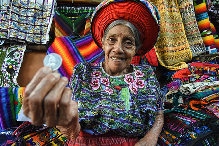An old Mayan woman seen holding a coin while selling traditional clothes in the region of Santiago Atitlan, Guatemala.